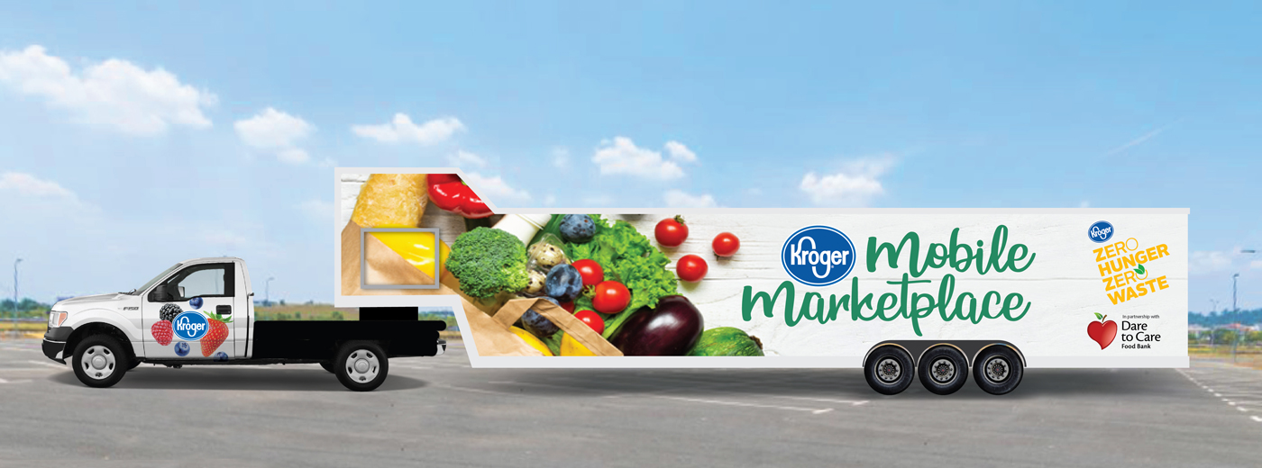 A truck decorated with the Kroger Mobile Marketplace logo and images of fresh food drives on a road with a clear sky in the background.