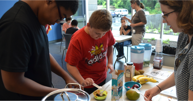 Individuals are engaged in preparing food with various ingredients and utensils on a table.