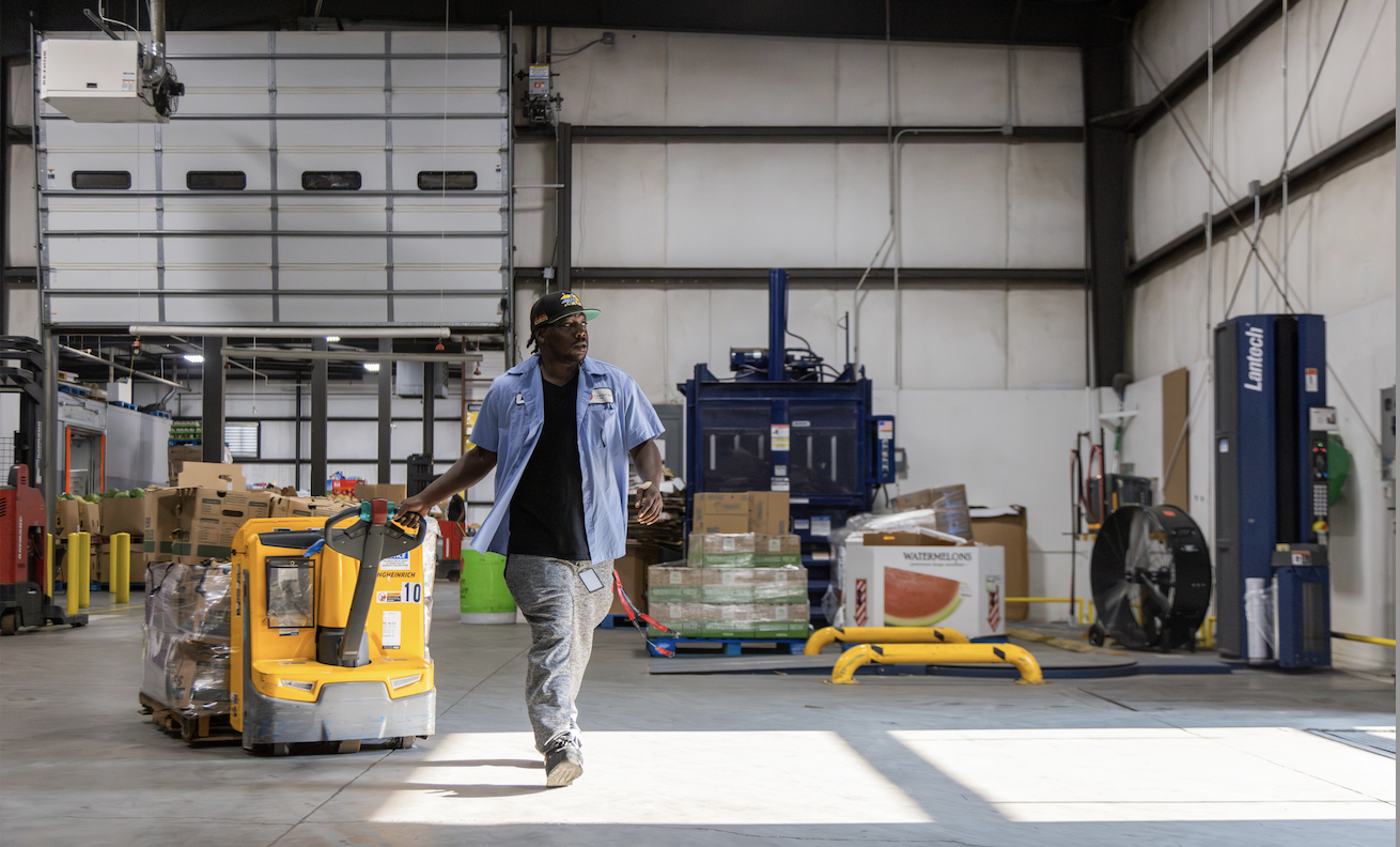 A worker is pulling a yellow manual pallet jack in a warehouse.