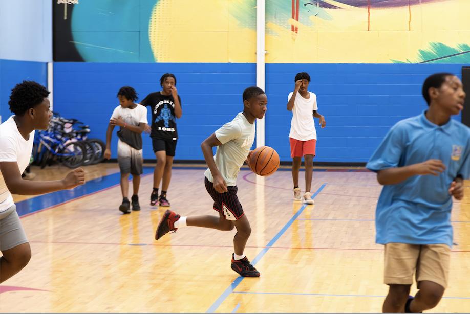 Individuals are engaged in a basketball activity in an indoor court with vibrant wall colors.