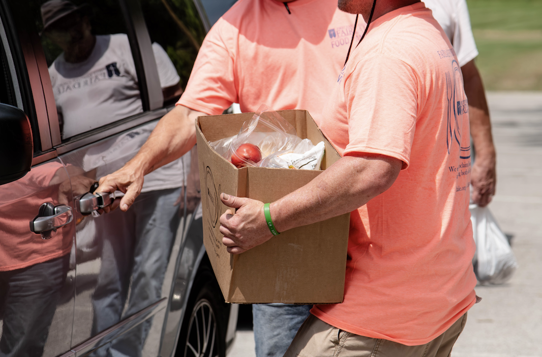 Two individuals in salmon-colored shirts are unloading a cardboard box from a vehicle.