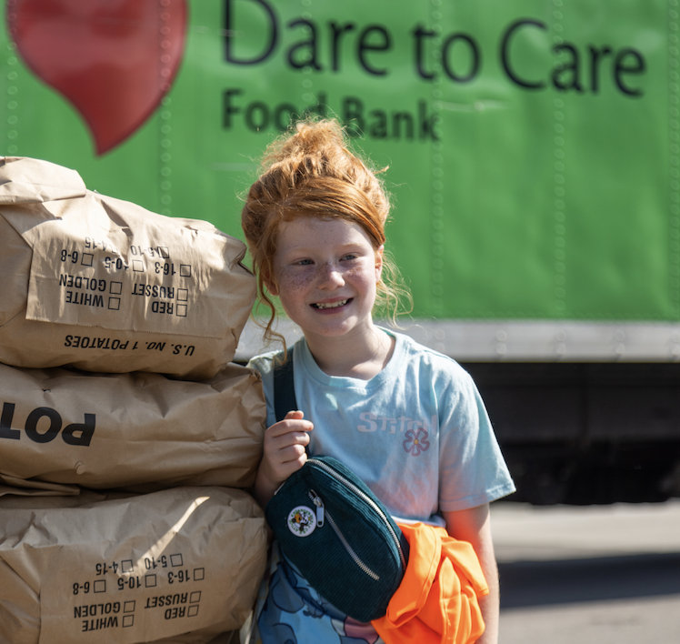 A smiling individual with red hair is holding a sack near a truck with 
