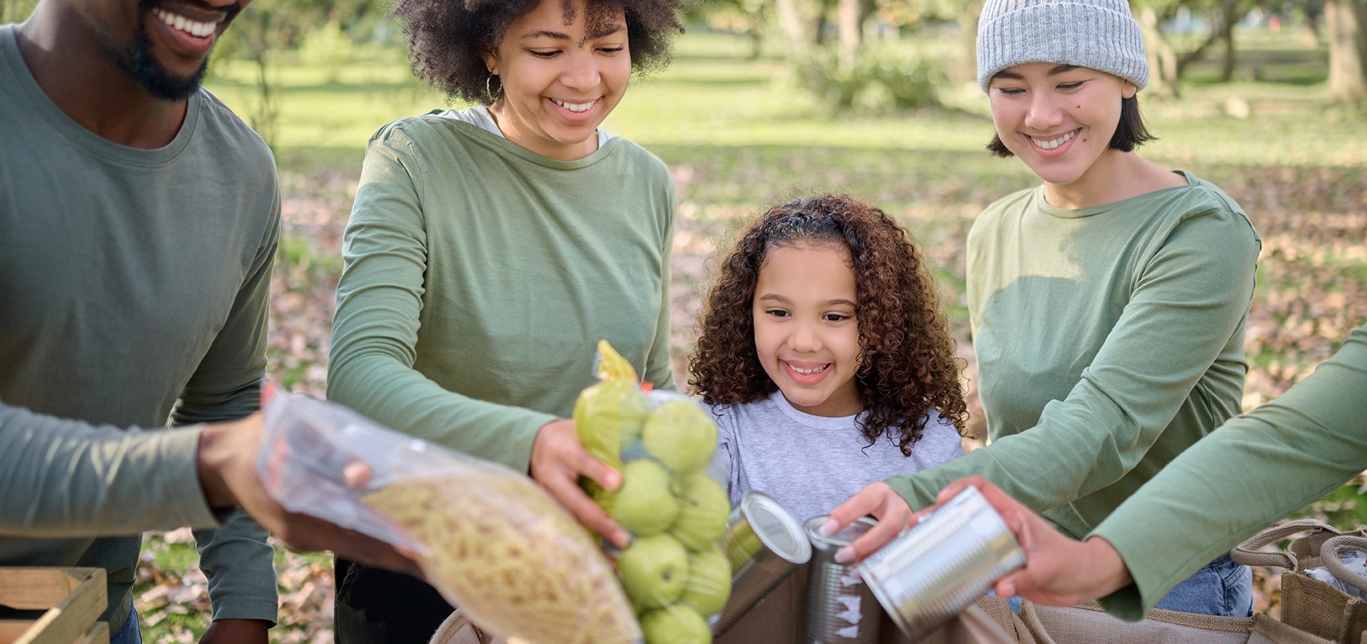 A happy family appears to be enjoying an outdoor activity together, with a focus on sharing and handling fresh produce and grocery items.